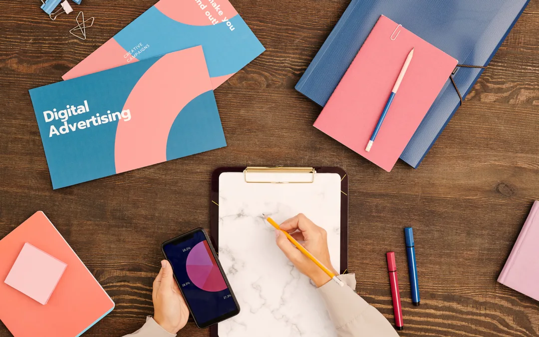 Flatlay of hands of young contemporary marketer with pencil over blank paper in clipboard surrounded by leaflets or books and notebooks